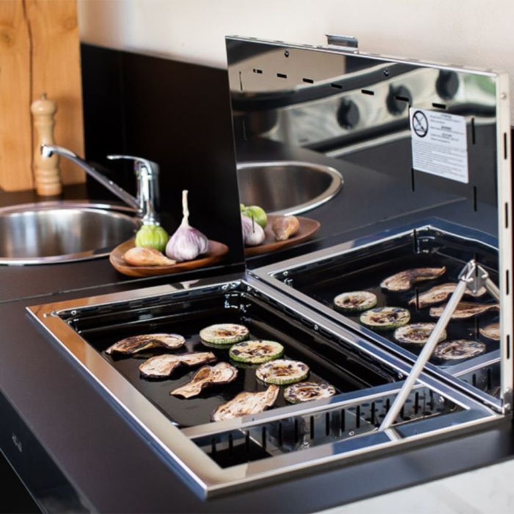 Plancha encastrable ANTIGUA au gaz ENO en utilisation, cuisant des légumes dans une cuisine extérieure.