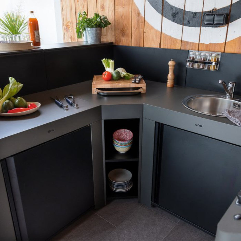 Cuisine extérieure équipée d'un meuble d'angle gris cargo ENO, combiné avec un évier et un réfrigérateur. Plan de travail spacieux et rangements intégrés pour une organisation optimale.
