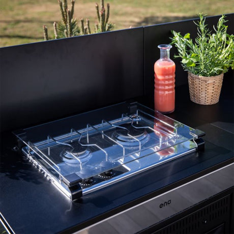 Gros plan sur la table de cuisson du Module Table MASTER Encastrée 80 cm Noir et Inox - ENO, avec couvercle en verre, herbes aromatiques et bouteille de jus en extérieur.