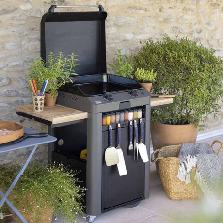 Plancha Gaz Fusion 60 sur chariot avec porte-épices et ustensiles, installée en extérieur.