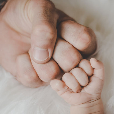 Main d’un père tenant celle de son bébé, symbole d’amour et de complicité – Idée pour célébrer la fête des pères et offrir un cadeau spécial.