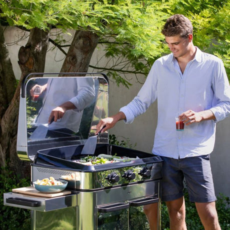 Homme utilisant la plancha gaz Enosign 80 en inox en extérieur, entouré de verdure. Idéale pour des repas conviviaux avec une cuisson précise et homogène.