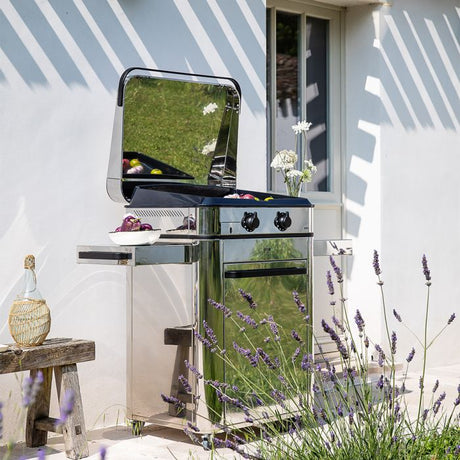 Plancha gaz ENOSIGN 65 sur chariot inox - ENO installée en extérieur, en pleine cuisson, avec des herbes et des légumes sous une pergola.